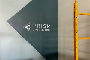 Prism Optometric's new lobby sign: acrylic sign with white letters on a painted grey triangle
