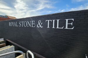 A close-up photo of the "Royal Stone & Tile" dimensional letters. The focus is on the smooth, metallic silver finish of the acrylic material, which reflects light and creates a polished look.