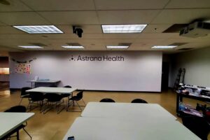 A wider view of Astrana Health's interior, showcasing the large-scale vinyl wall decal. Its colors and design complement the lobby sign, extending the brand throughout the space.