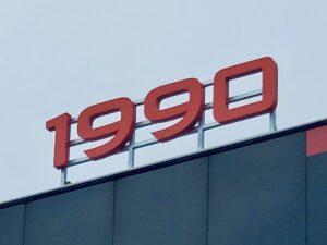 Red illuminated channel letters spelling "1990" mounted on a modern building with a silver aluminum base.