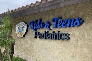 A channel letters sign reading 'Kids & Teens Pediatrics' on a textured wall.