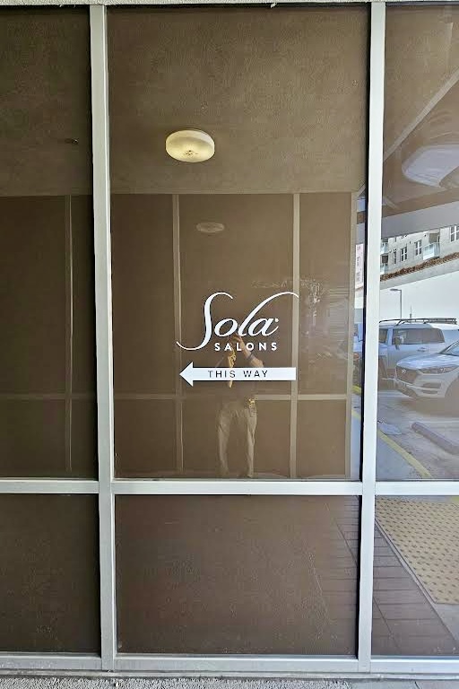 Minimalist white vinyl decal of Sola Salon's logo on a storefront window.