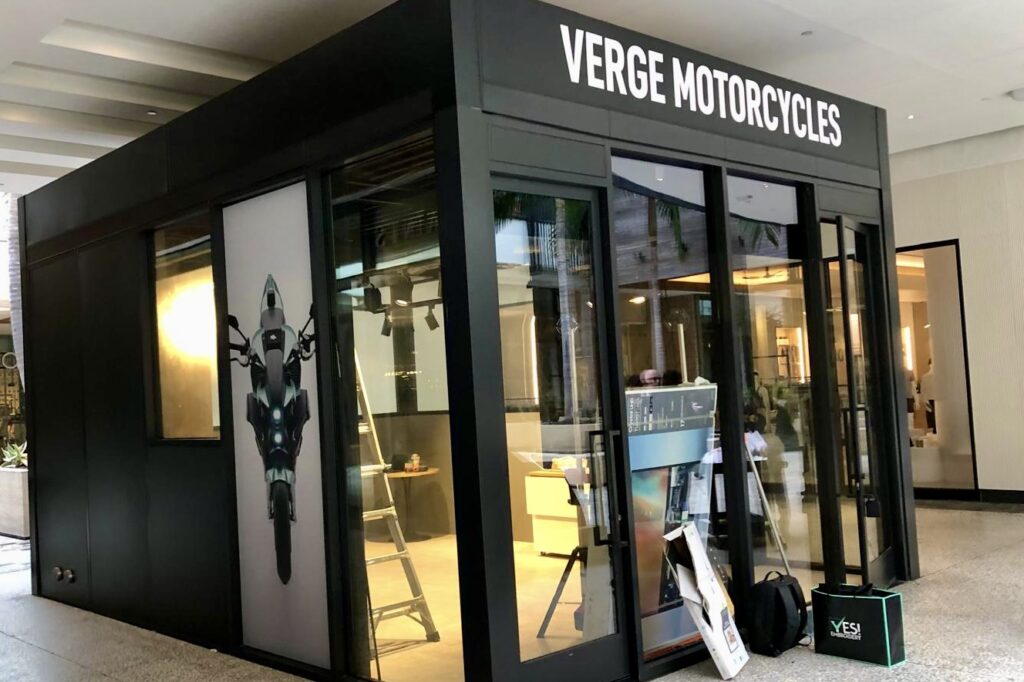 A photo of the Verge Motorcycles cubical exterior showcasing the dimensional letter sign mounted above the entrance. The clean white letters stand out against the dark background, creating a modern and sophisticated look.
