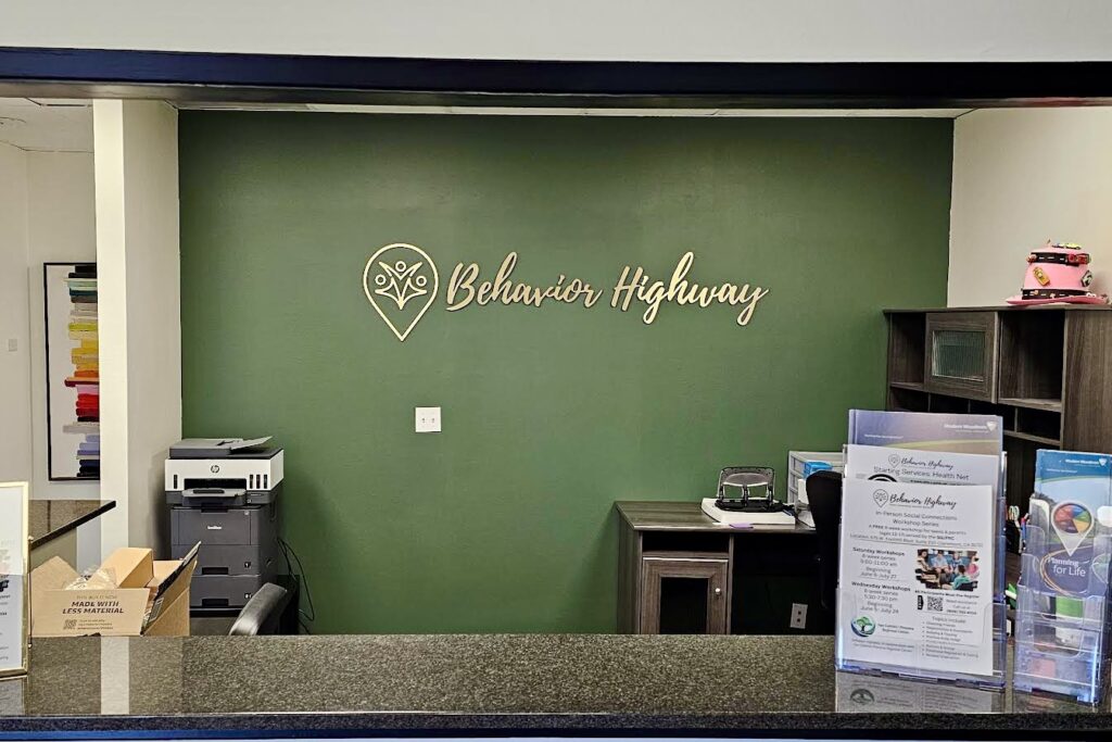 A photo of the Behavior Highway lobby sign mounted on a wall. The photo showcases the entire sign, highlighting the black acrylic base with brushed gold laminate faces and the prominent display of the company name and logo.