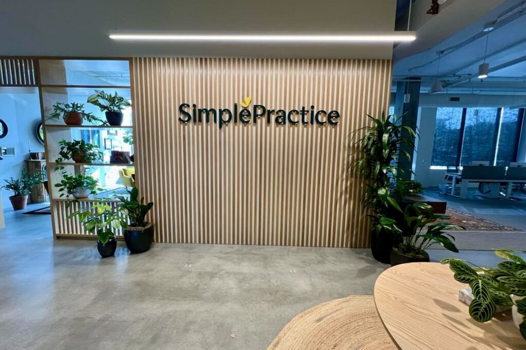 A close-up view of the Simple Practice lobby sign, showcasing the painted acrylic construction, two-size lettering, and integrated logo.