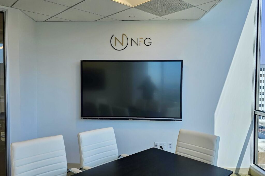 A wide shot of the oversized NFG logo sign mounted on a wall. The large size and brushed gold finish create a striking visual impact.