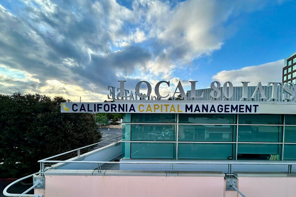 A  view of the California Capital Management illuminated sign. The sign features silver metallic lettering pushed through a white acrylic face, illuminated by a white LED light system.
