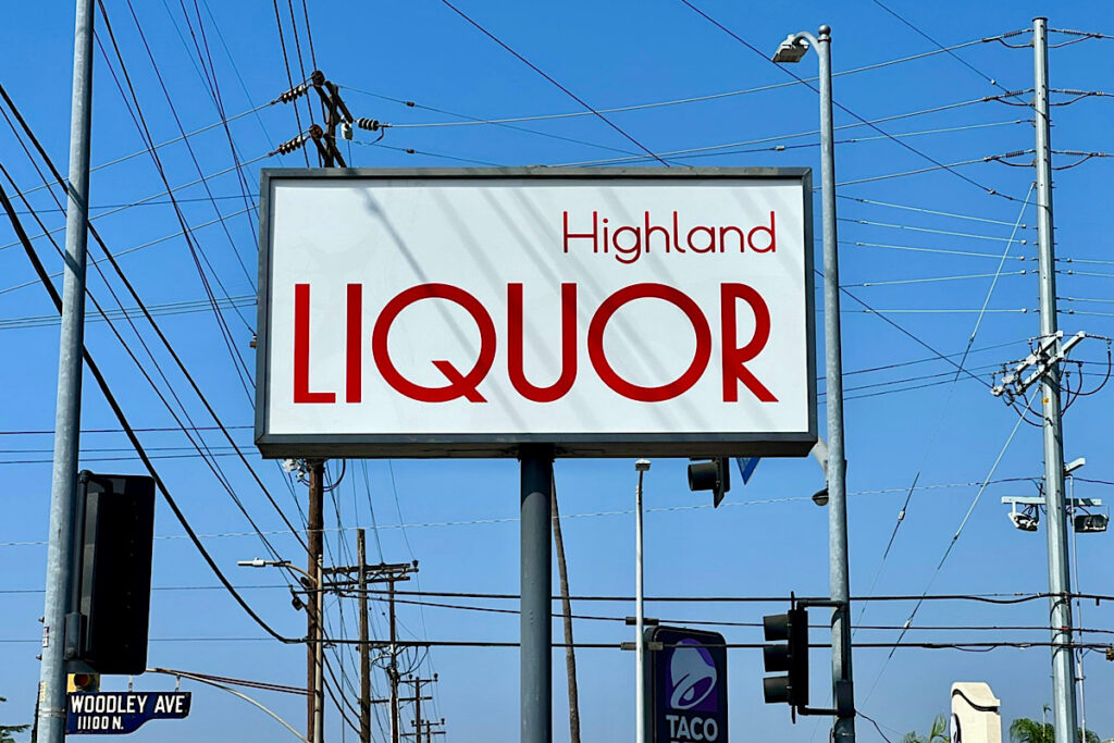 A wide shot of the Highland Liquor storefront featuring the two custom pole signs. The signs are prominently displayed on either side of the entrance, adding a vibrant touch to the facade.
