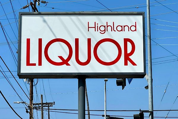 A close-up view of one of the Highland Liquor pole signs. The sign features red vinyl lettering on a white background, with the words “Highland Liquor” prominently displayed.
