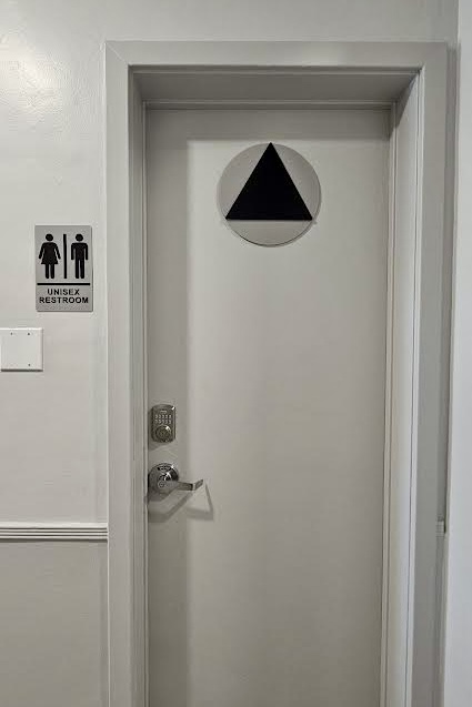 A close-up view of a restroom door sign and a corresponding wall sign. The signs are made of silver acrylic and feature black lettering that complies with California Title 24 accessibility regulations.
