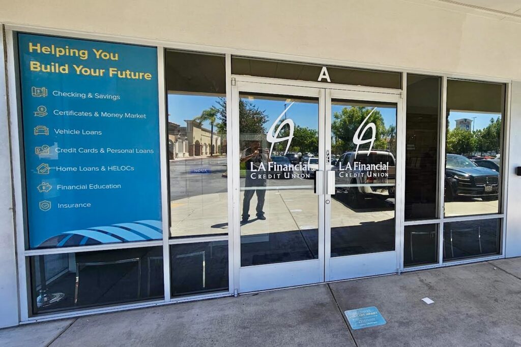 An expansive view of LA Financial's Norwalk branch exterior. Bespoke window displays adorn the front windows. The left pane prominently showcases the LA Financial emblem, while the right pane likely illustrates key financial services offered by the branch.
