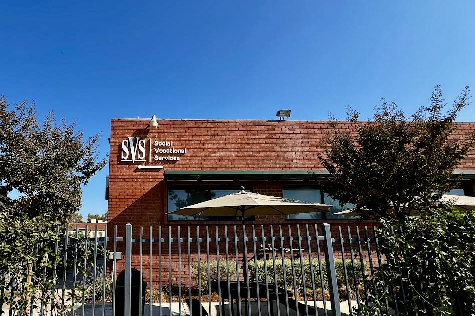 An image of a wide-angle sign made of stainless steel that reads "Social Vocational Services" in raised-dimensional letters. (Whittier location)