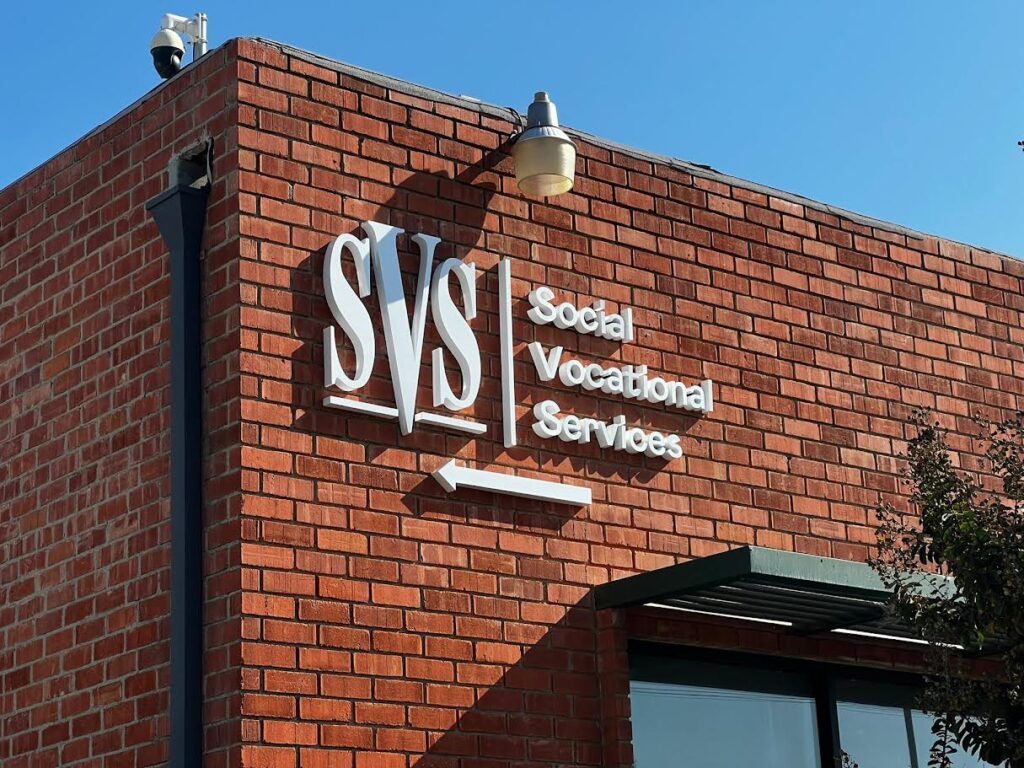 Wide-angle view of a fabricated stainless steel sign with the words "Social Vocational Services" written in raised, three-dimensional characters. (Whittier location)