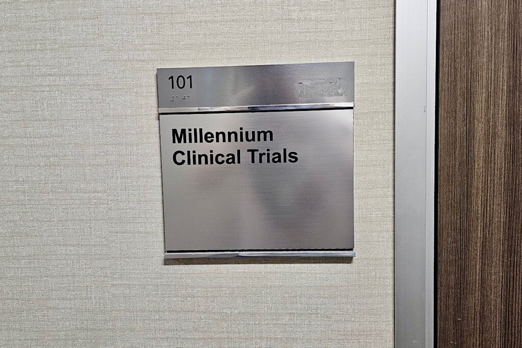 A close-up view of the suite plaque insert text. The text “Millennium Clinical Trials” is displayed in a clear, bold font.
