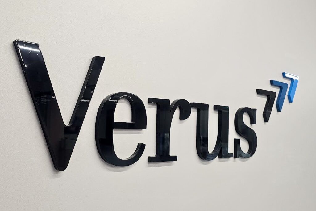 Close-up view of dimensional letters spelling "Verus" mounted on an office wall. The letters are painted in the company's brand colors and feature a clean, professional font.