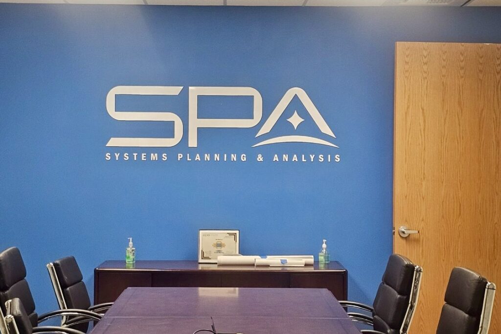 Close-up of the Systems Planning & Analysis boardroom sign, showcasing the sharp acrylic lettering and logo.